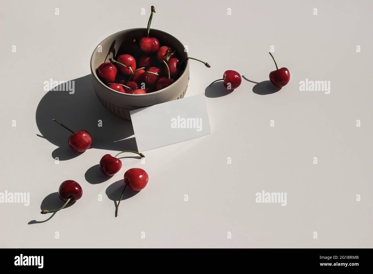 Modern food still life composition. Ceramic Bowl of red cherries on beige table background in sunlight. Blank business card mock ups scene. Top view Stock Photo