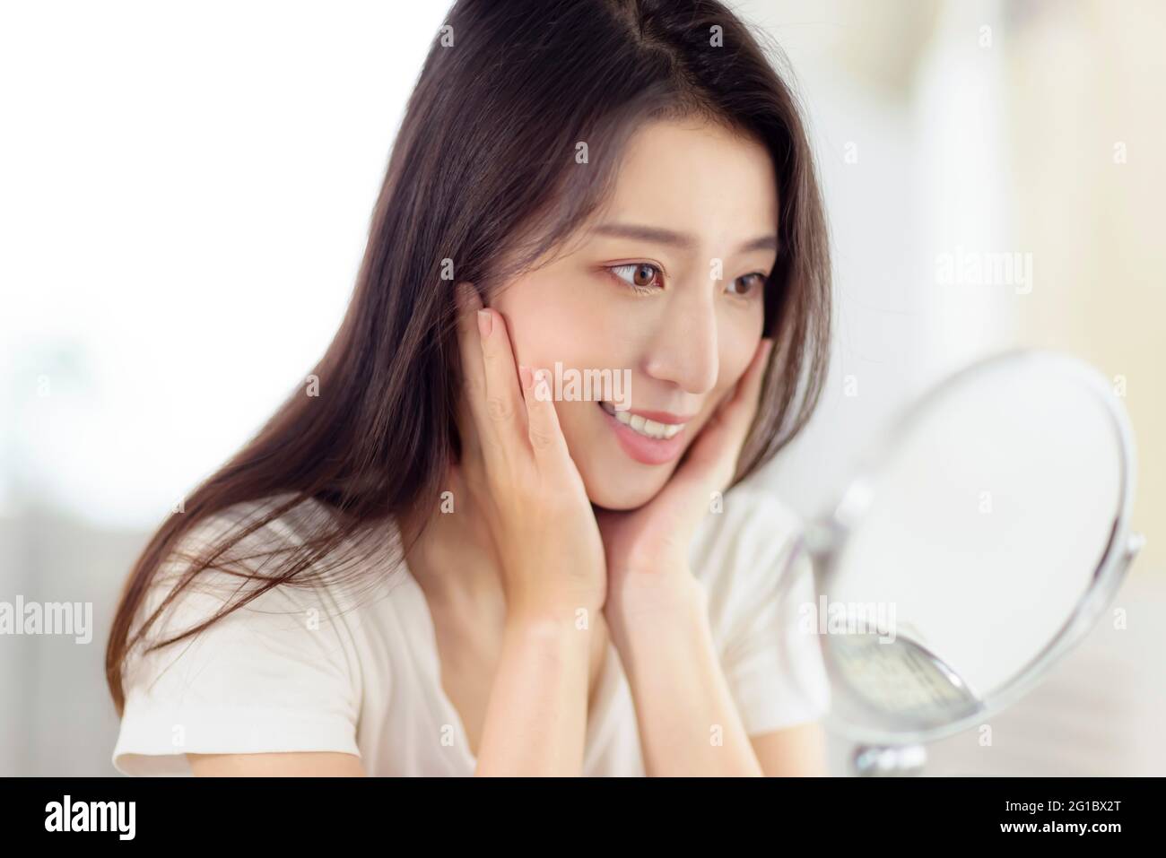 Asian young woman looking at her face in mirror Stock Photo
