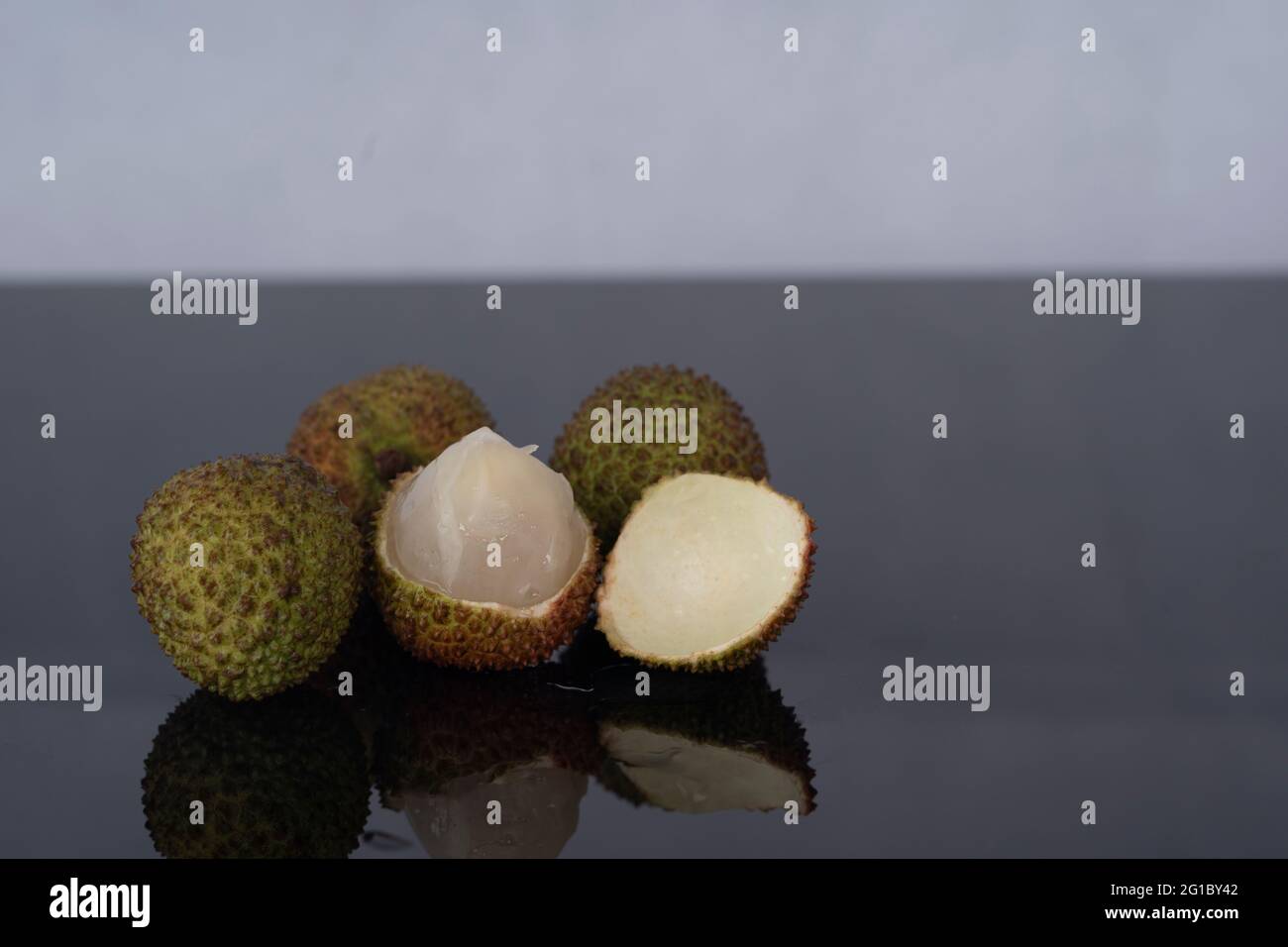 A bunch of ripe green lychees with one peeled fruit. Selective focus points. Blurred background Stock Photo