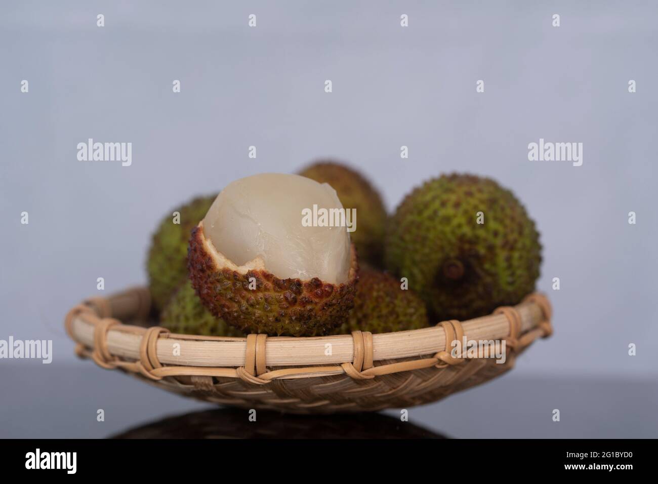 A bunch of ripe green lychees with one peeled fruit. Selective focus points. Blurred background Stock Photo