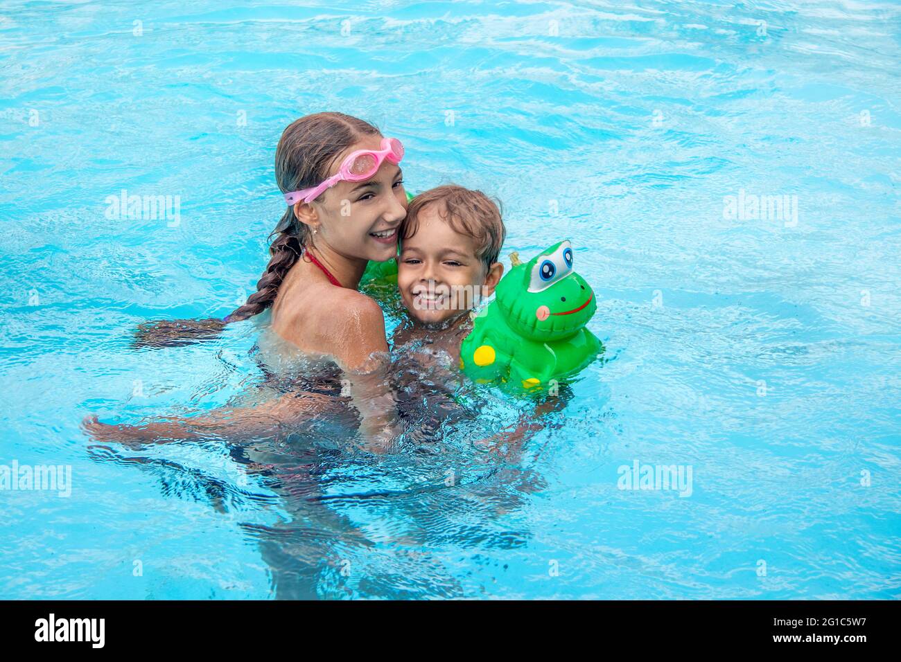 Happy brother and sister swim in the pool. Smiling girl and boy are