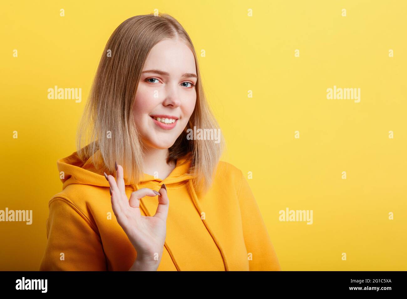 Portrait young woman shows ok hand gesture. Teenage blonde calm smiling girl shows positive ok gesture symbol like and approval isolated on color Stock Photo