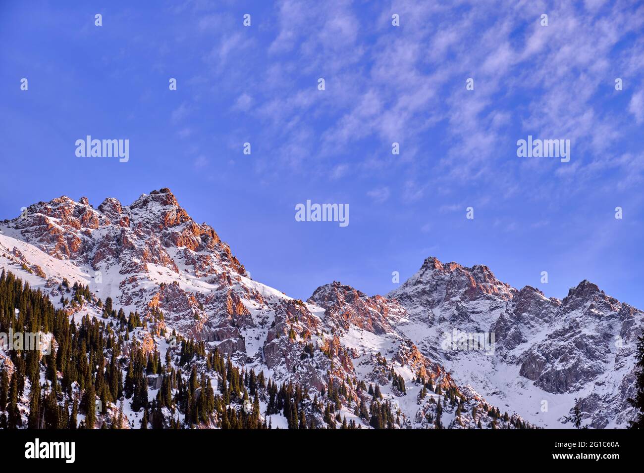 Majestic rocky peaks with fir forest against a blue sky with clouds at sunset in the winter season Stock Photo