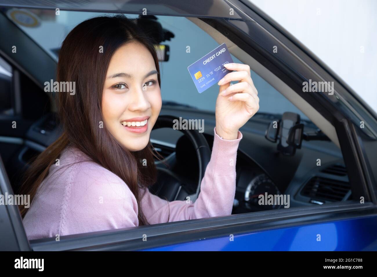 Happy beautiful Asian woman sitting inside new car blue and showing credit card pay for oil, pay a tire, maintenance on the garage, Make payment for r Stock Photo