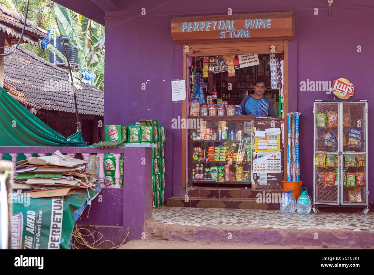 Indian vendor stands behind counter selling snacks, toiletries and provisions at Perpetual Wine Store, Agonda, Goa, India Stock Photo