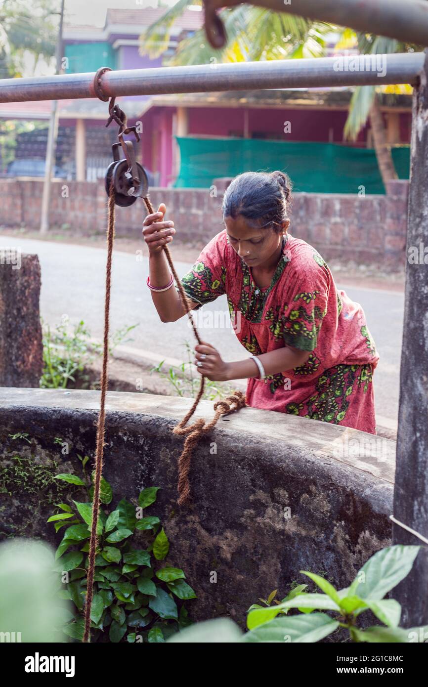 Indian female draws water from well using traditional rope and pulley system, Agonda, Goa, India Stock Photo