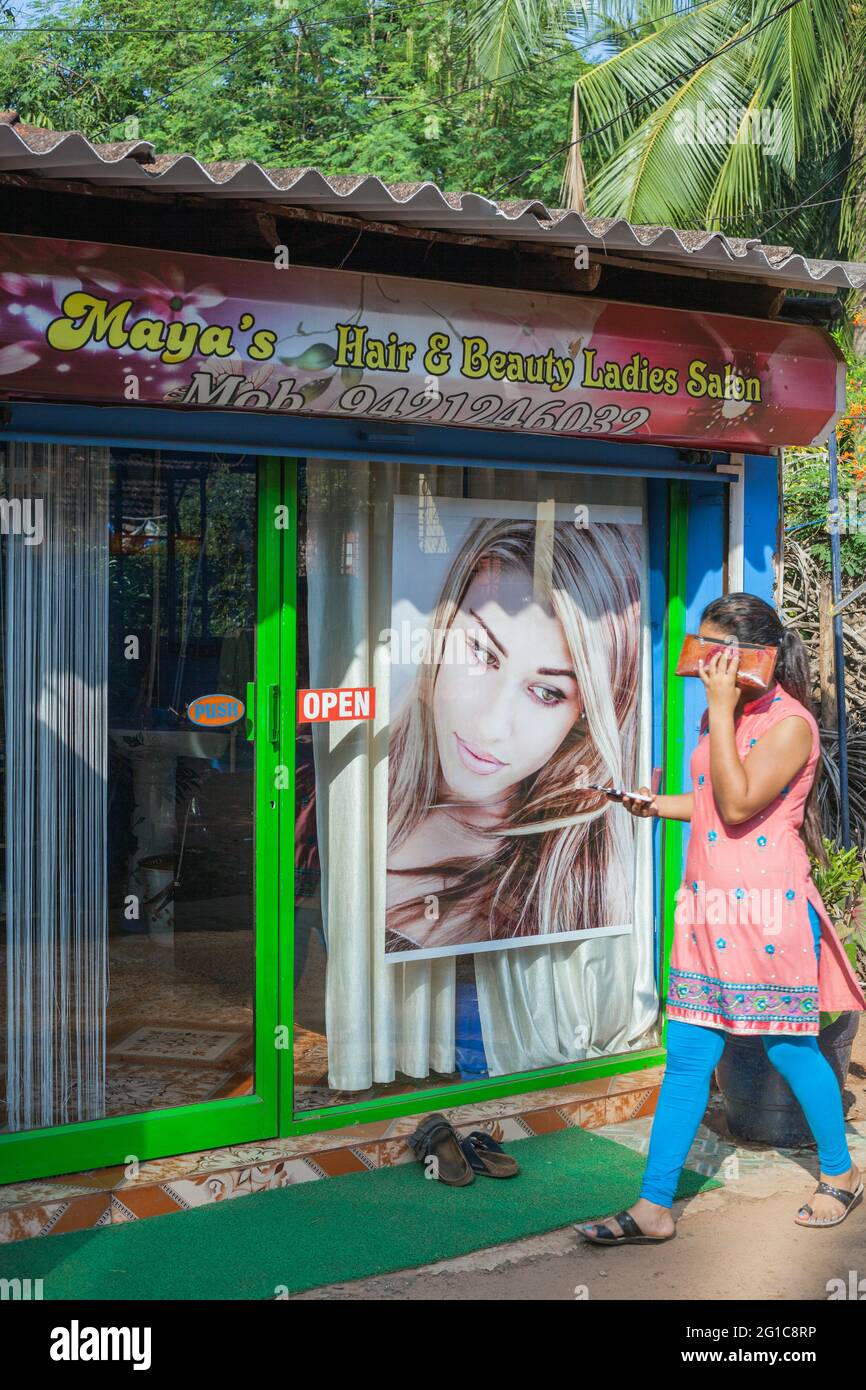 Indian female shielding face from sun walking to the entrance of Maya's Hair & Beauty Ladies Salon, Agonda, Goa, India Stock Photo