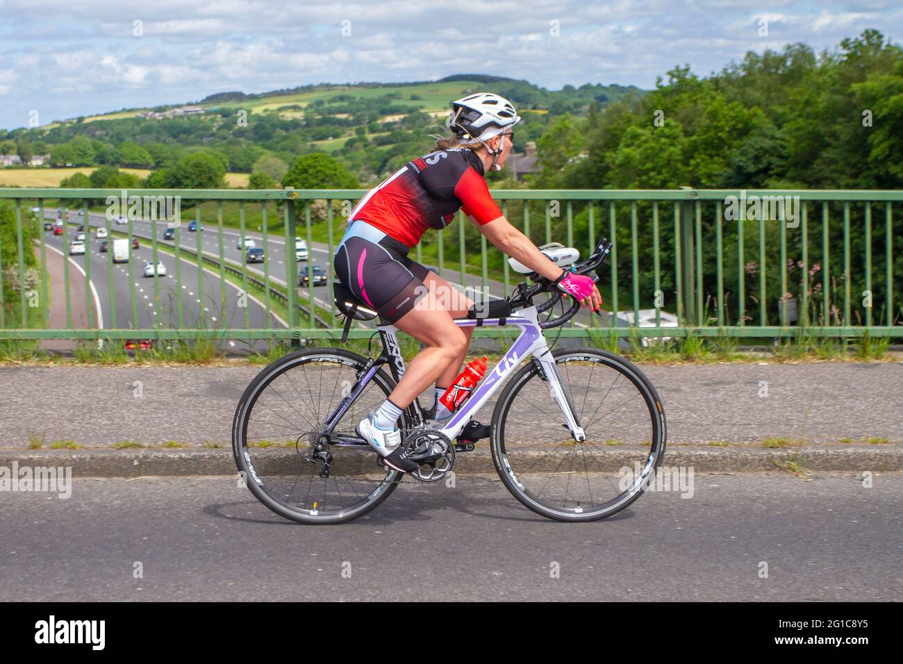 Femal cyclist riding Liv sports road bike on countryside route crossing motorway bridge in rural Lancashire, UK Stock Photo