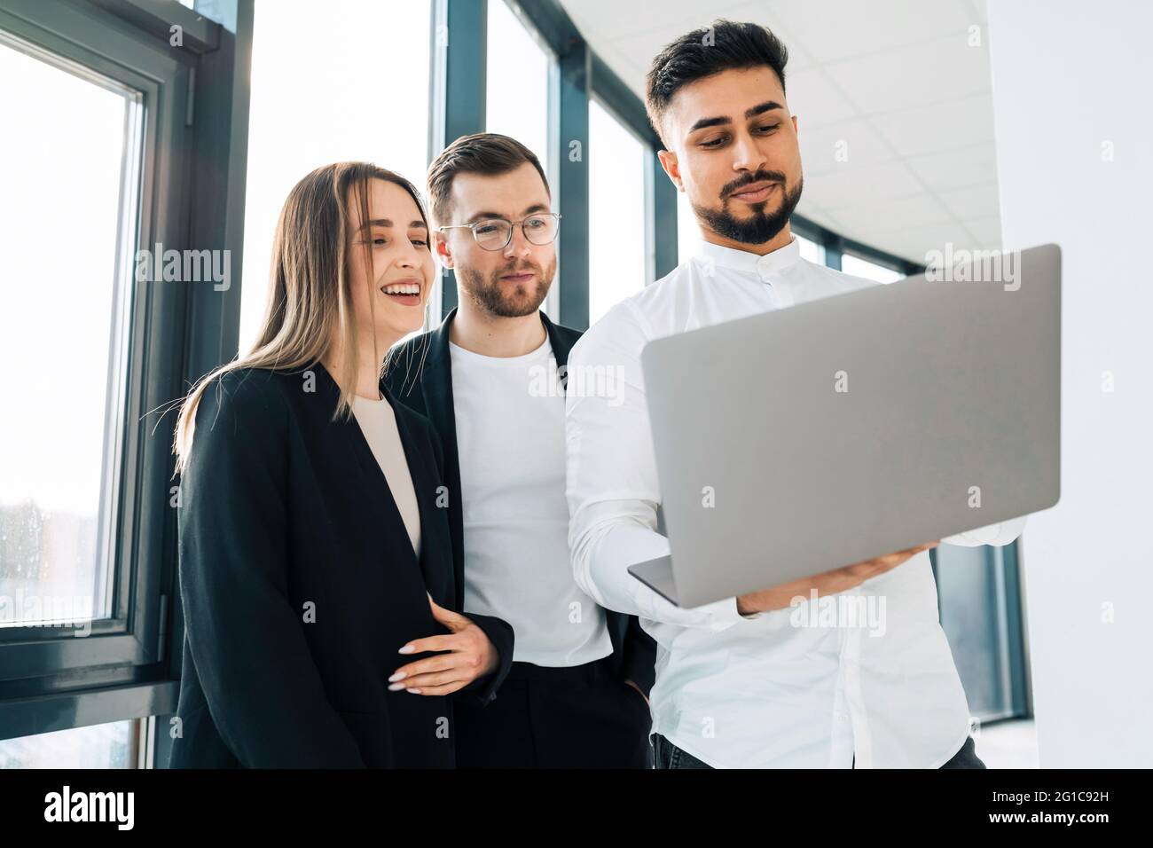 Three office workers looking at a laptop discussing the company's growth rate Stock Photo