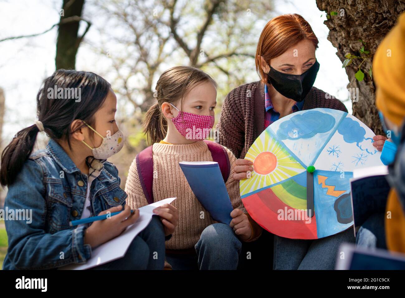 Teacher with small children sitting outdoors in city park, learning group education and coronavirus concept. Stock Photo