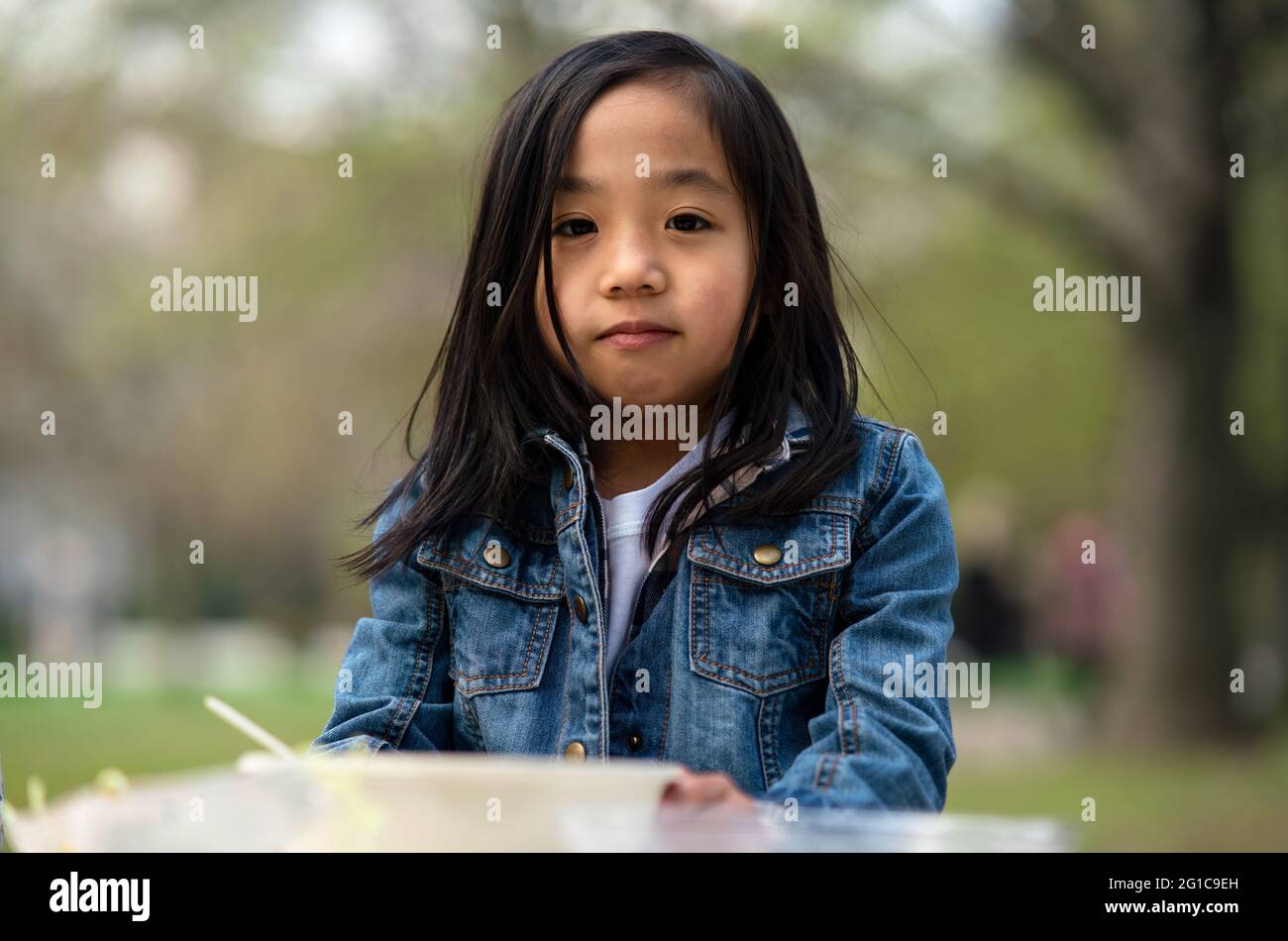 Small child looking at camera outdoors in city park, learning group education concept. Stock Photo