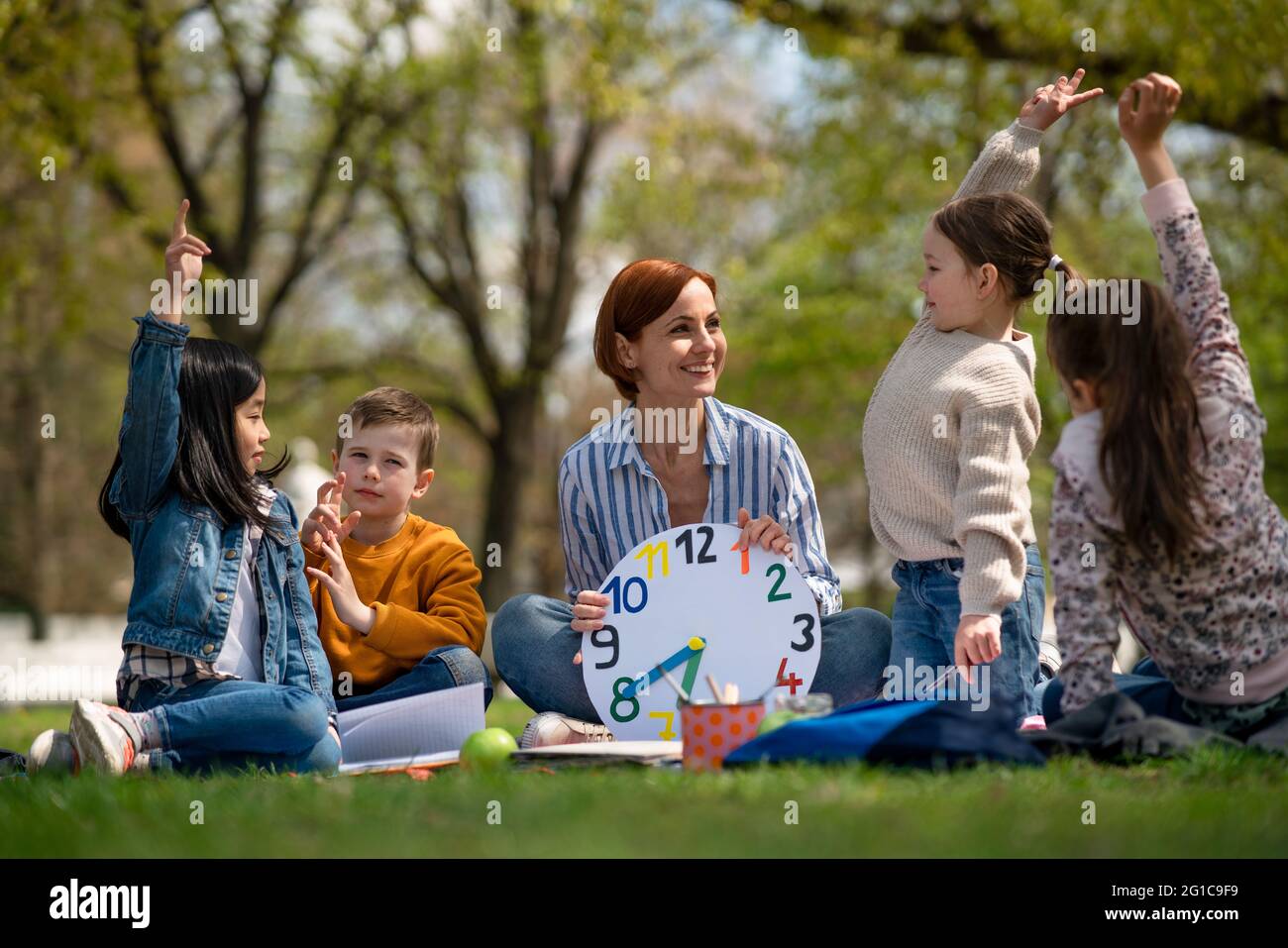 Teacher with small children sitting outdoors in city park, learning group education concept. Stock Photo