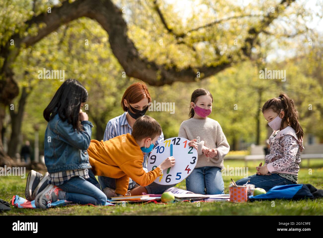 Teacher with small children sitting outdoors in city park, learning group education and coronavirus concept. Stock Photo