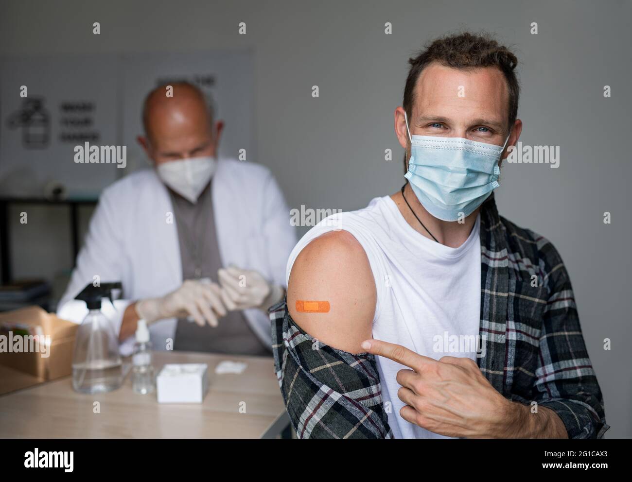Happy mid adult man after covid-9 vaccination, pointing to plaster on arm and looking at camera. Stock Photo