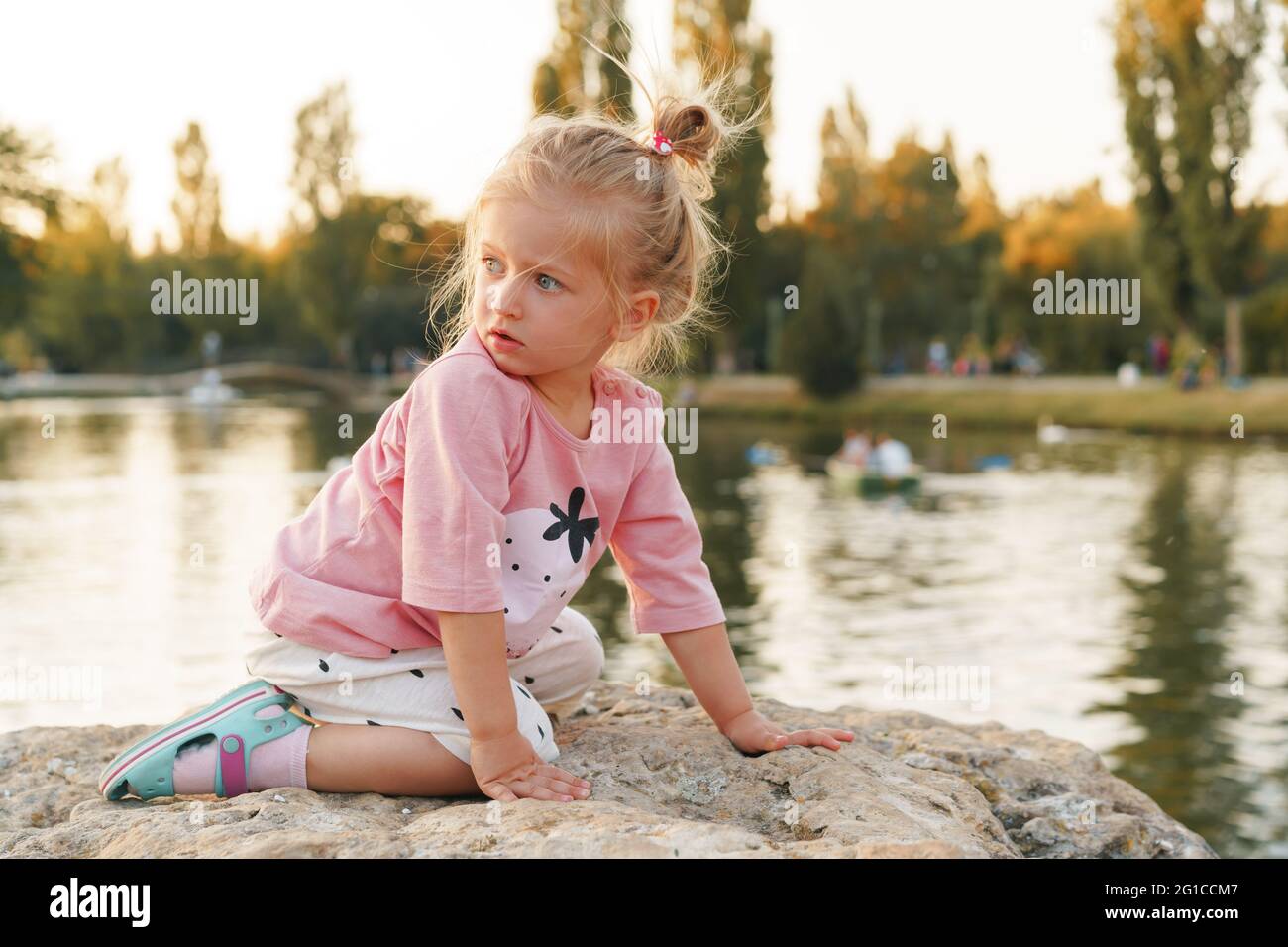 Little girl sitting on a huge stone in park near the lake Stock Photo ...