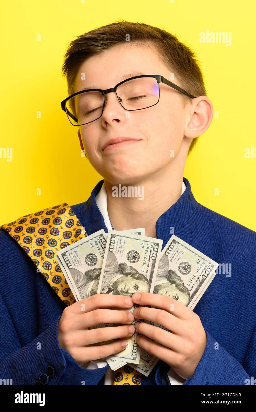 A boy in glasses and an oversized suit with a satisfied face is holding