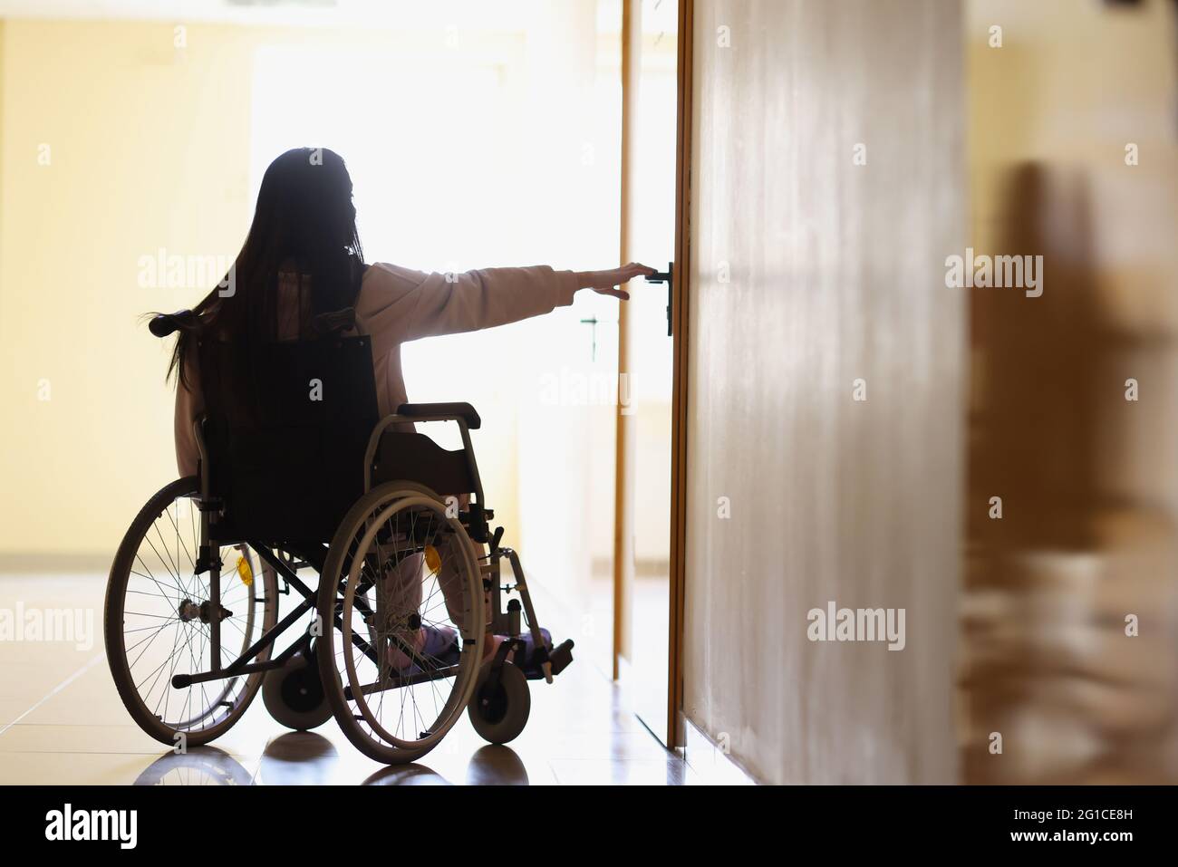 Woman in wheelchair reaches out to open handle of door in dark hallway