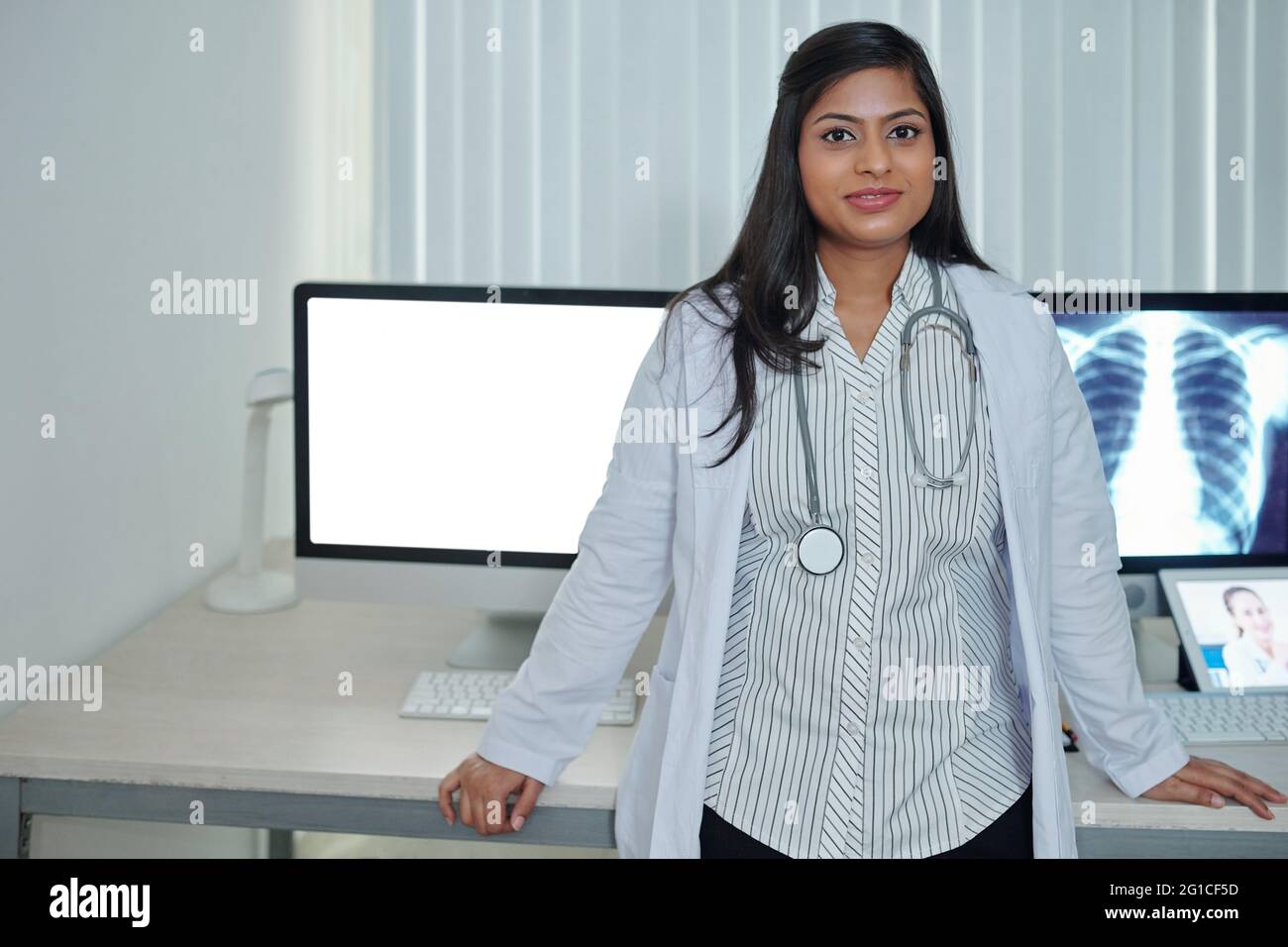 Portrait of smiling young female physician standing at office desk with