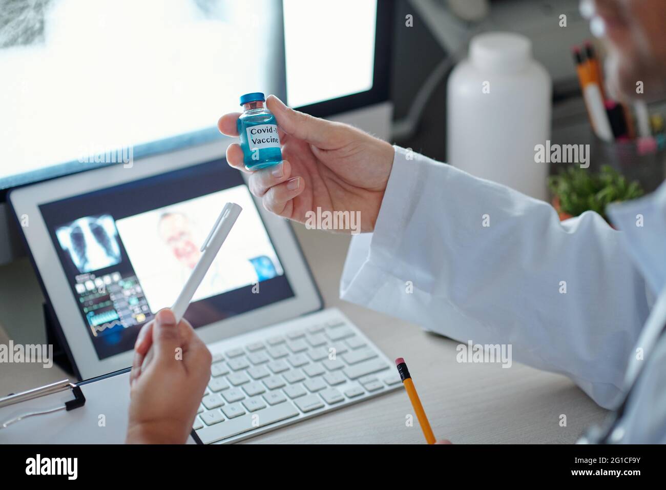 Hands of doctors having online meeting with coworker from another clinic and discussing properties of vaccine against coronavirus Stock Photo