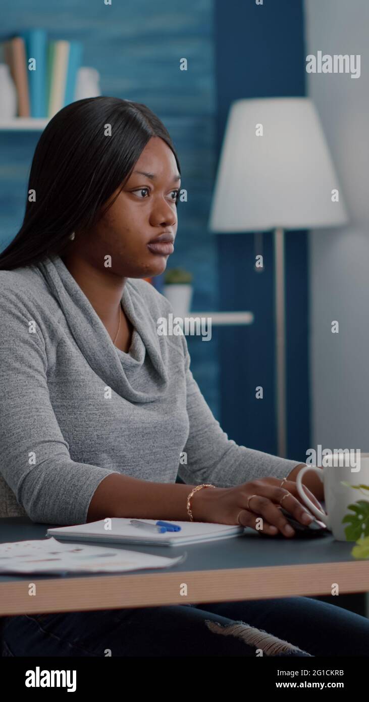 African american student with dark skin working remote from home at marketing online course using elearning university platform. Computer user sitting at desk table in living room browsing information Stock Photo