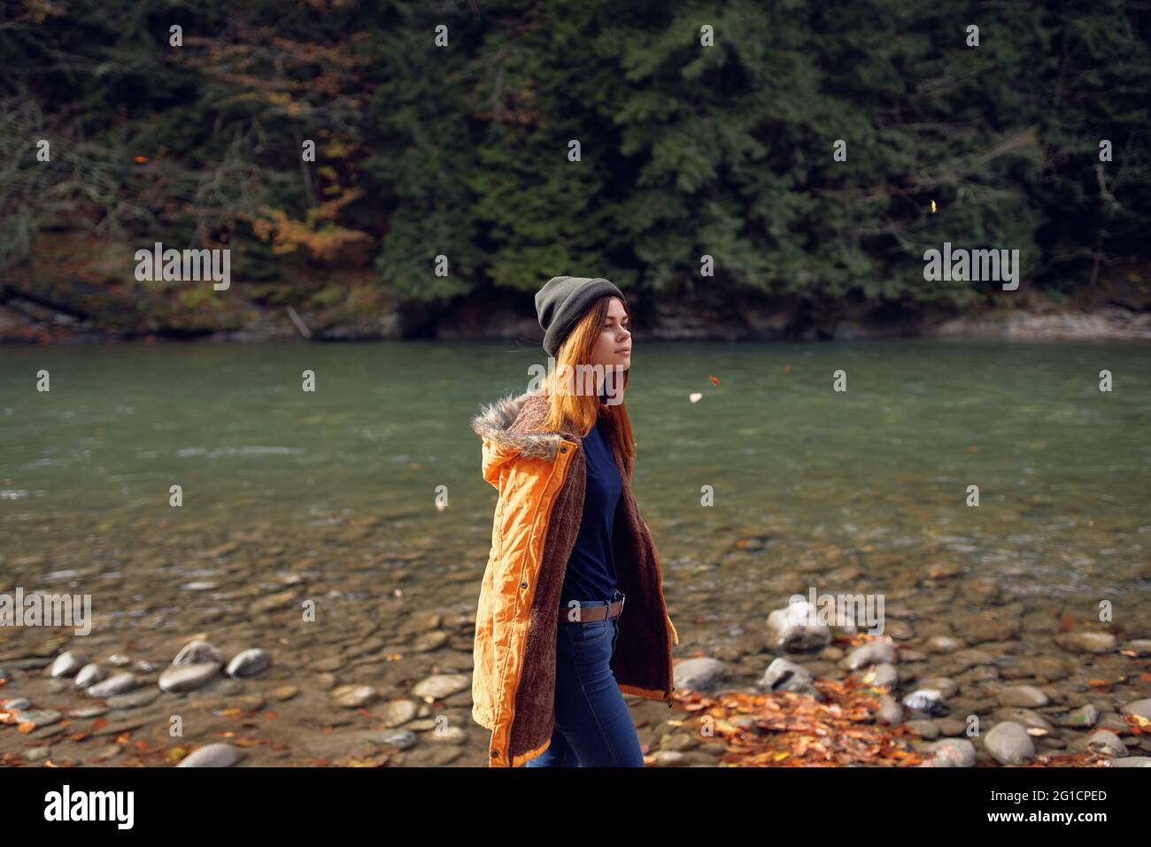 woman in a yellow jacket near the river admires nature Autumn forest ...