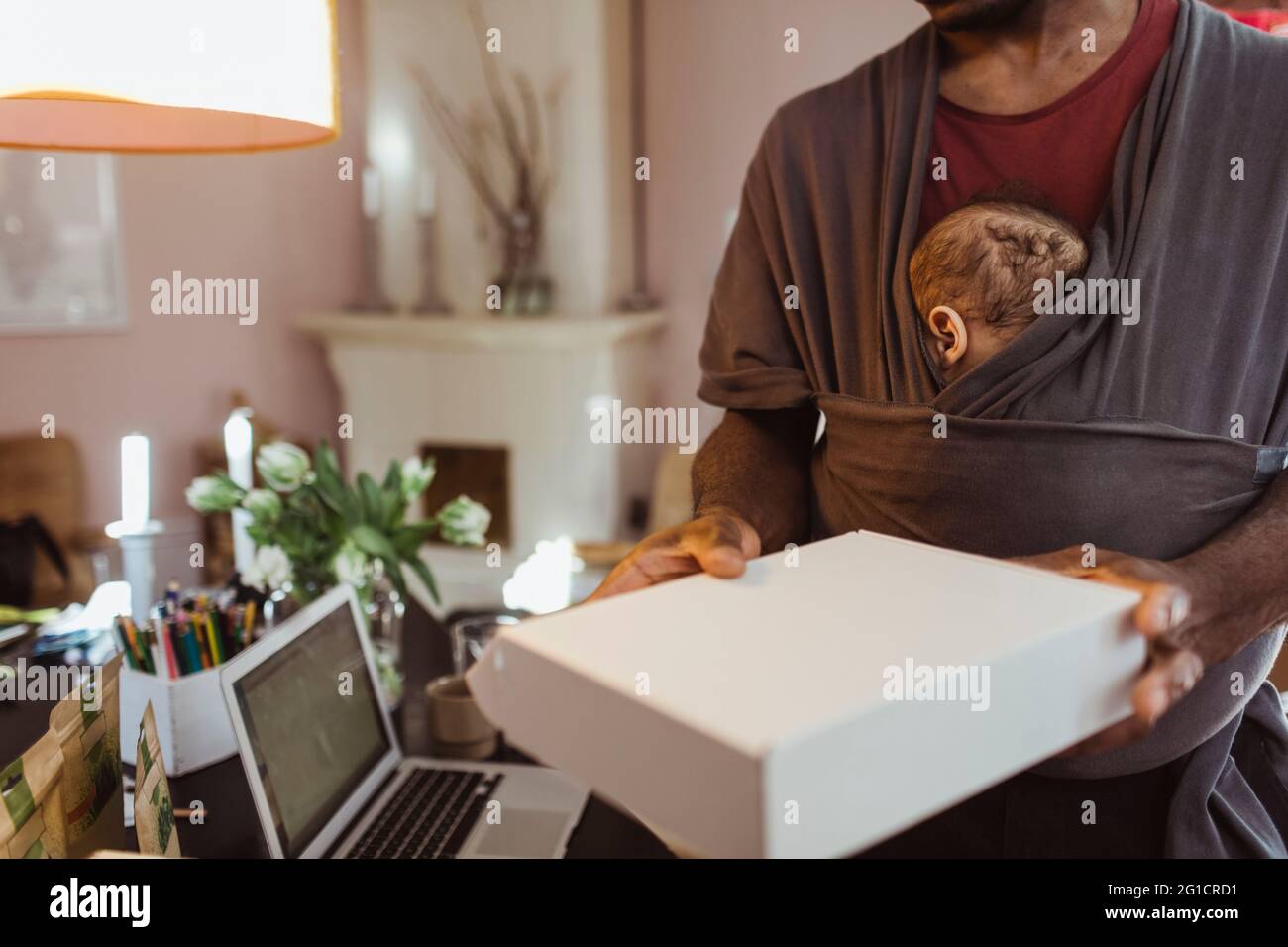 Midsection of businessman holding box with son in baby carrier at home office Stock Photo