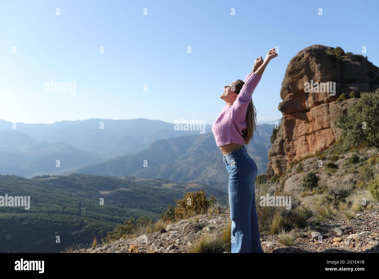 Side view portrait of an excited woman celebrating vacation raising arms in the mountain Stock Photo