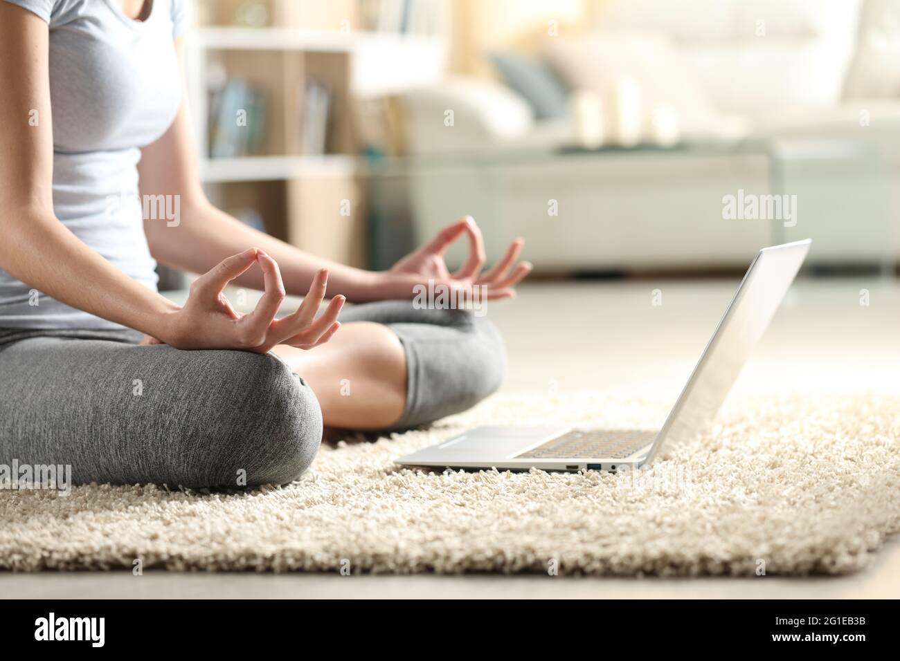 Close up of a woman doing yoga exercise watching online video tutorial on laptop at home Stock Photo