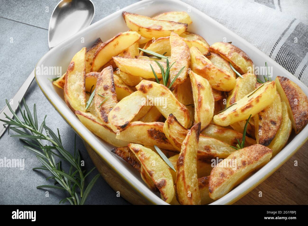 Crispy roast potatoes with fresh rosemary leaves in baking dish on gray background. Stock Photo