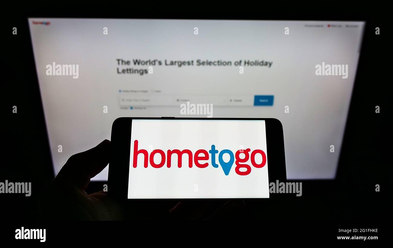 Person holding smartphone with logo of German accommodation search engine HomeToGo GmbH on screen in front of website. Focus on phone display. Stock Photo