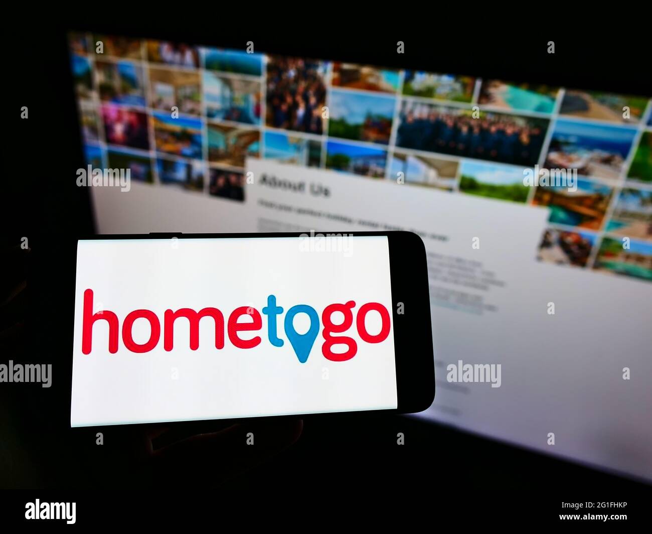 Person holding cellphone with logo of accommodation search engine HomeToGo GmbH on screen in front of business webpage. Focus on phone display. Stock Photo