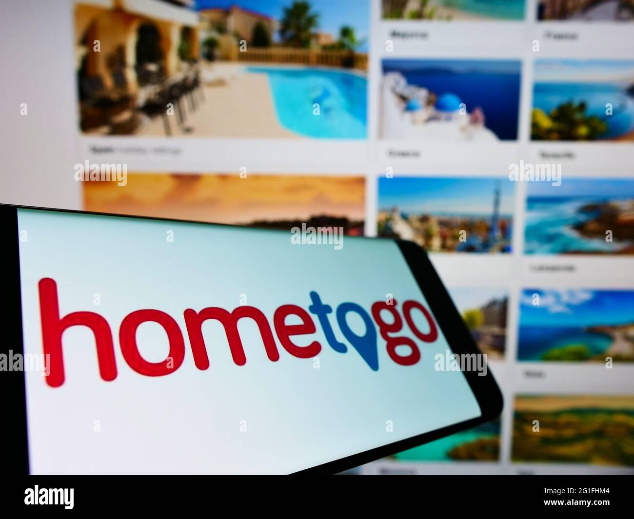 Smartphone with logo of German accommodation search engine HomeToGo GmbH on screen in front of website. Focus on center-left of phone display. Stock Photo