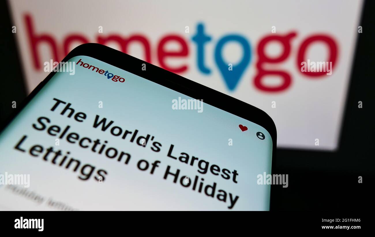 Mobile phone with website of German accommodation search engine HomeToGo GmbH on screen in front of logo. Focus on top-left of phone display. Stock Photo