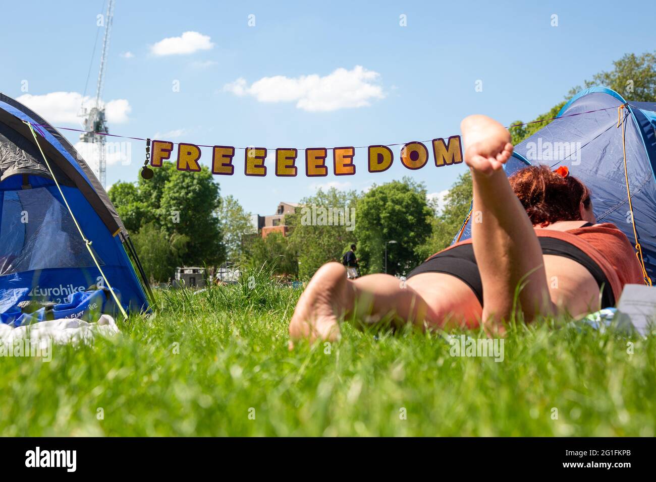 A young woman chilling in the grass at a freedom protest on Shepherd's Bush Green, London, UK. May 2021 Stock Photo