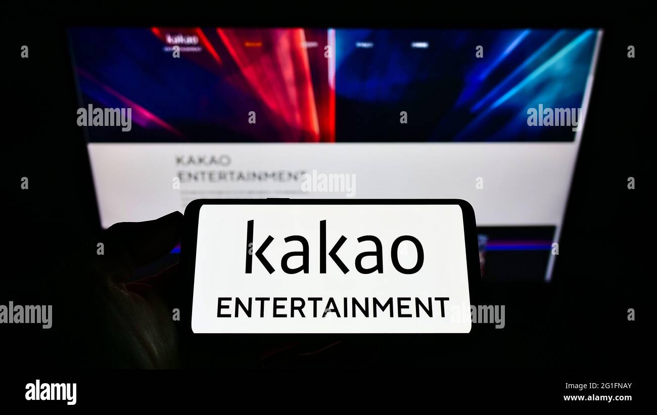 Person holding smartphone with logo of South Korean company Kakao Entertainment Corp. on screen in front of website. Focus on phone display. Stock Photo