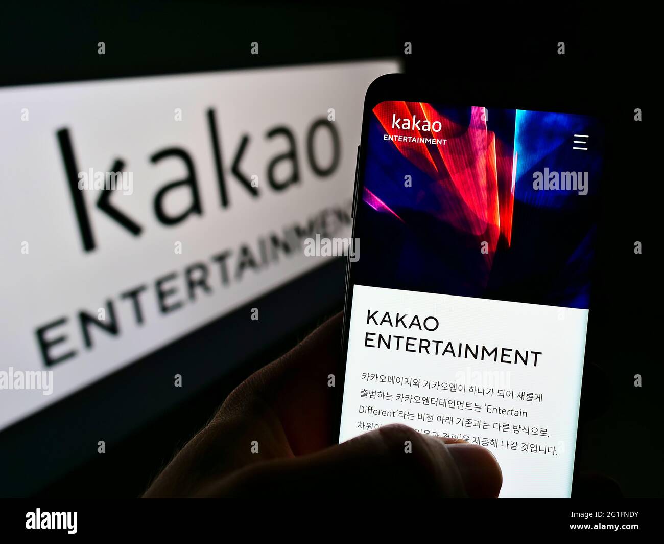 Person holding mobile phone with webpage of South Korean company Kakao Entertainment Corp. on screen with logo. Focus on center of phone display. Stock Photo