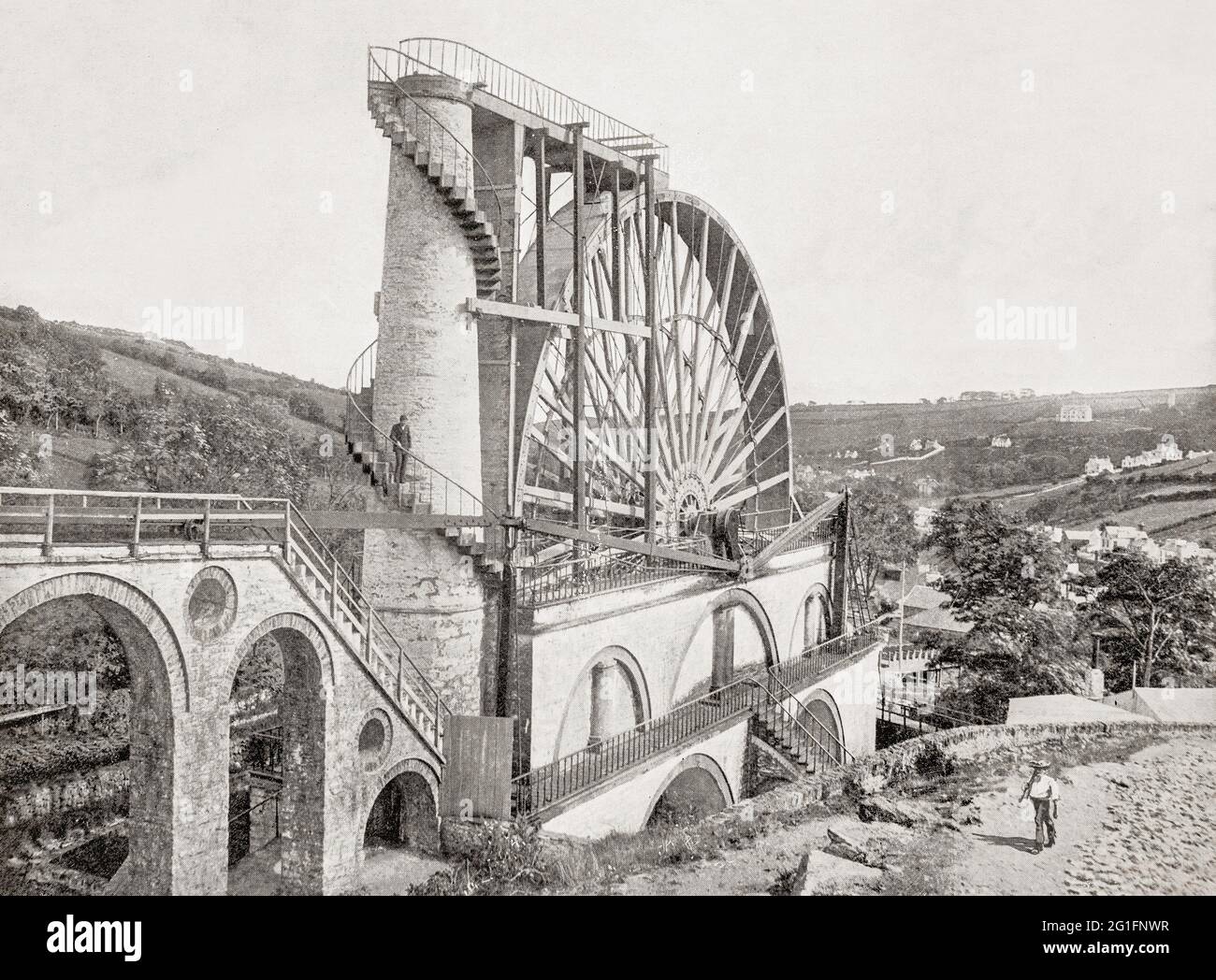 A late 19th century view of Laxey Wheel (also known as Lady Isabella) is built into the hillside above the village of Laxey in the Isle of Man. The largest working waterwheel in the world with a 72-foot-6-inch (22.1 m) diameter, revolving at approximately three revolutions per minute. It was designed by Robert Casement in 1854 to pump water from the Great Laxey Mines industrial complex, employing over 600 miners at its peak, producing lead, copper, silver and zinc, until it closed in 1929. Stock Photo