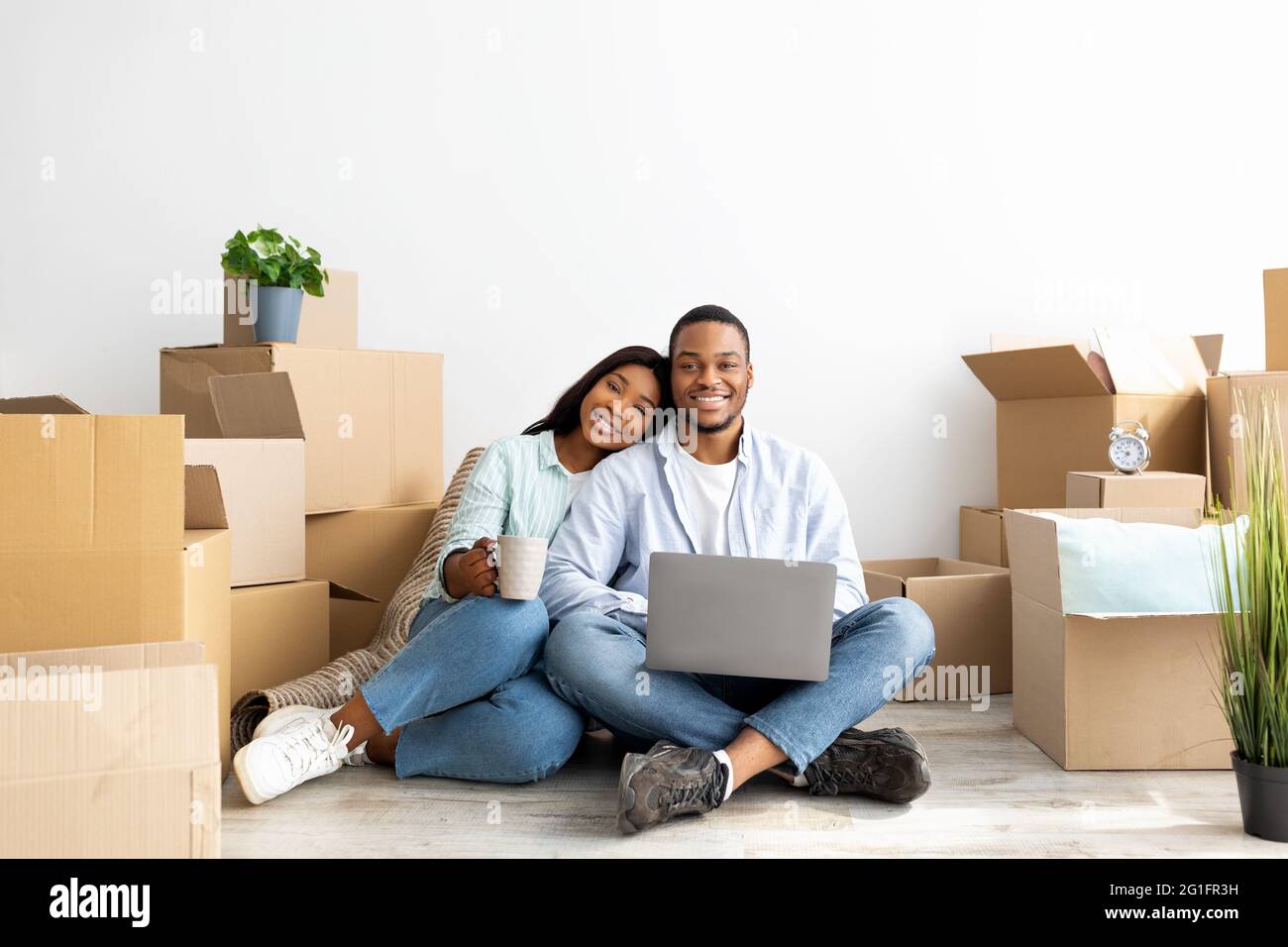 Moving concept. Happy african american couple purchasing furniture for new apartment, sitting on floor and using laptop Stock Photo