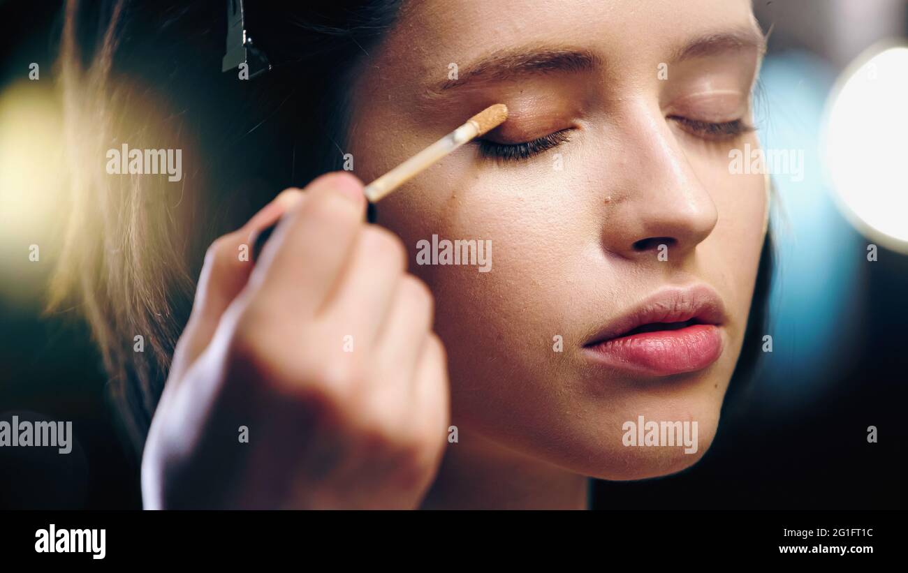 makeup artist applying concealer on eyelid of young woman Stock Photo