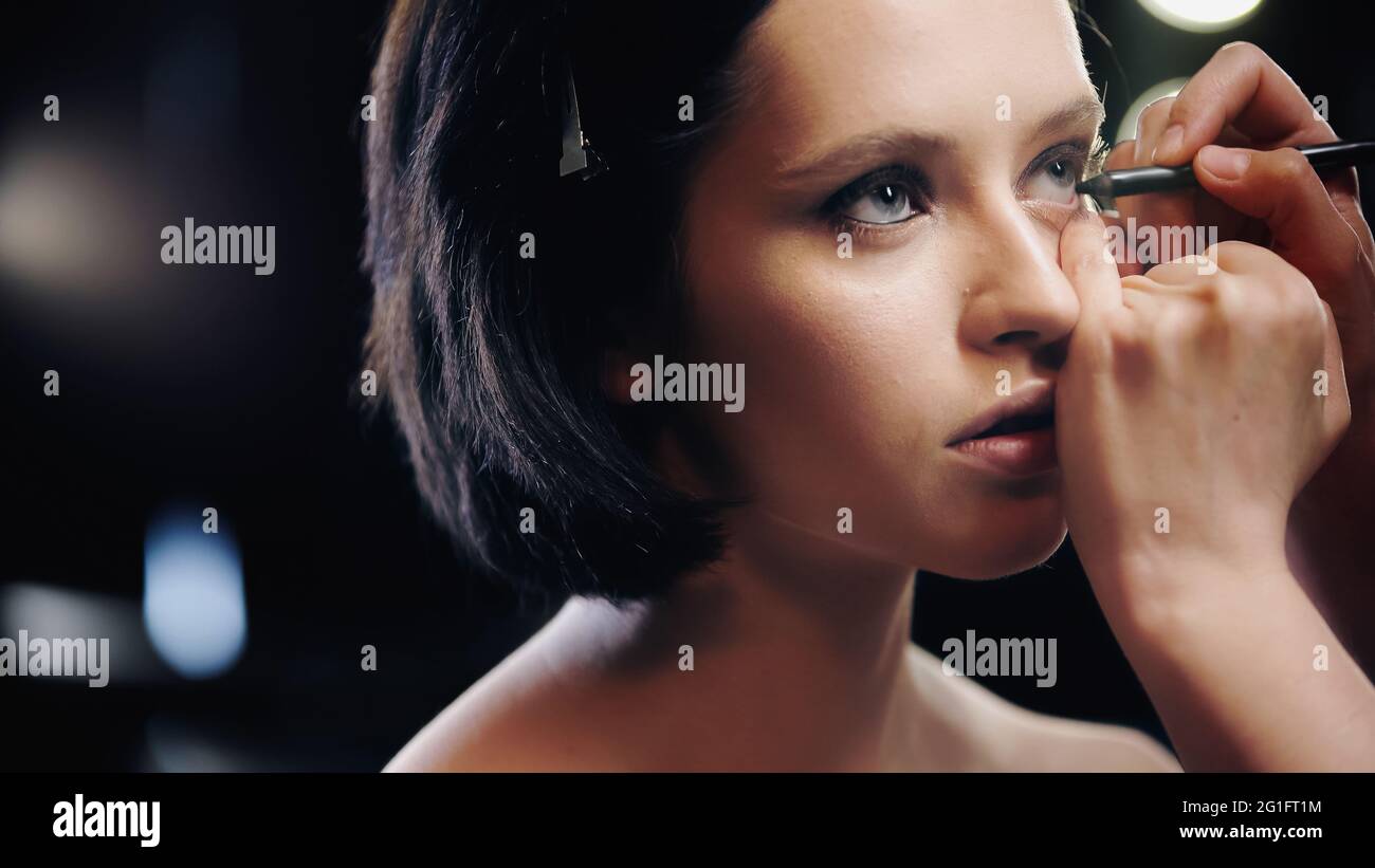 make up artist applying black eyeliner on lower eyelid of woman Stock