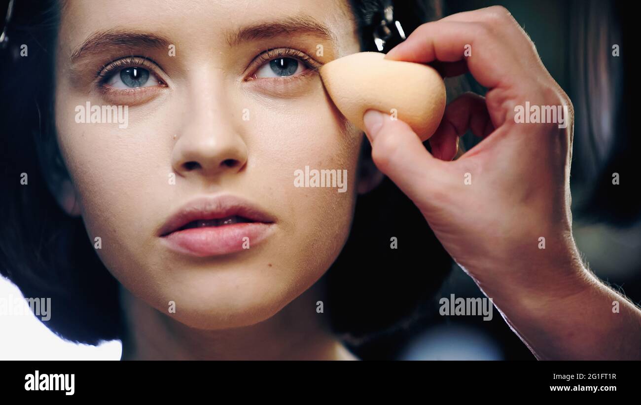 makeup artist applying makeup foundation with cosmetic sponge on skin of pretty model Stock Photo