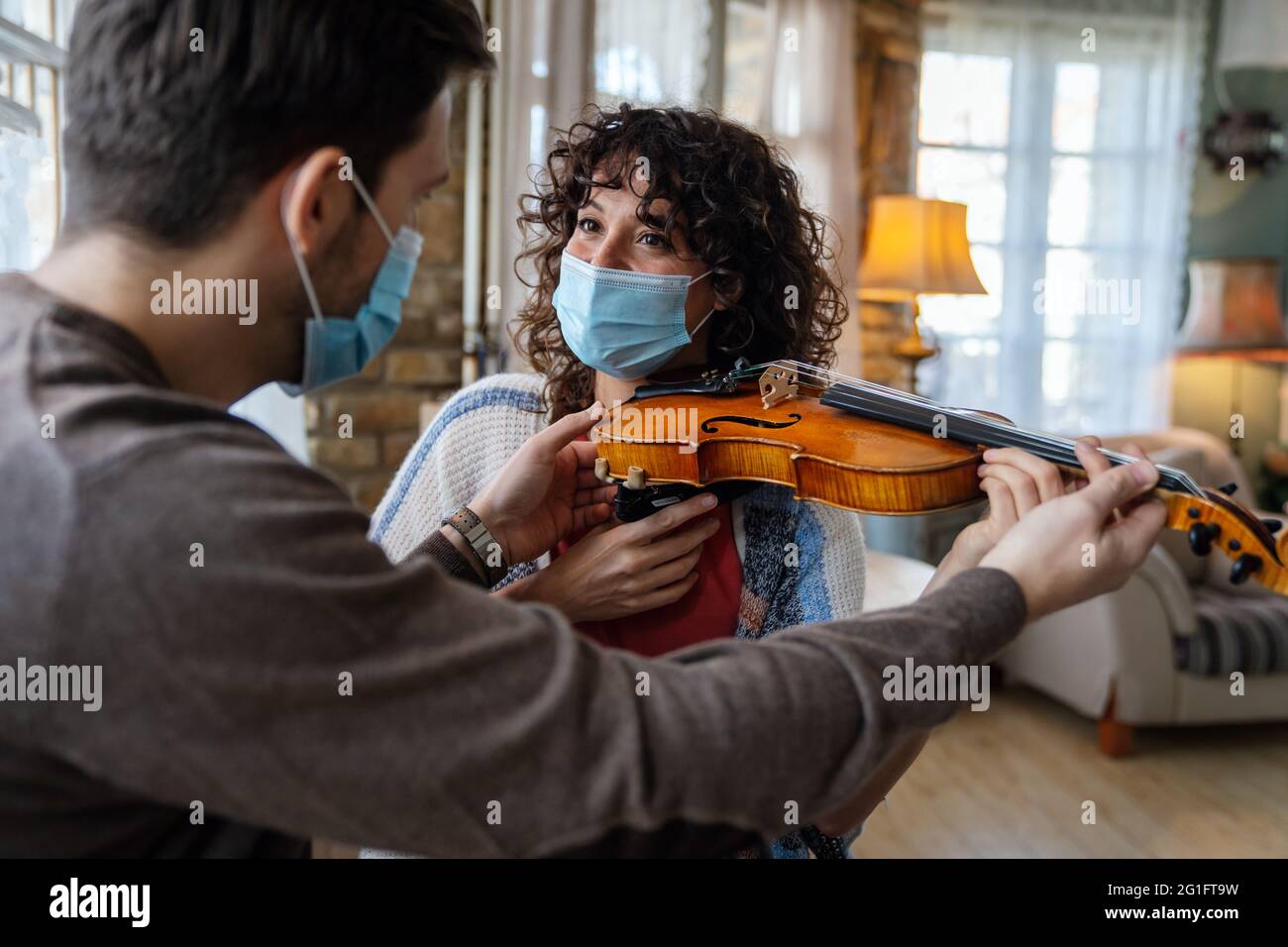 Happy woman play violin under music teacher's instructions in mask during coronavirus at home Stock Photo
