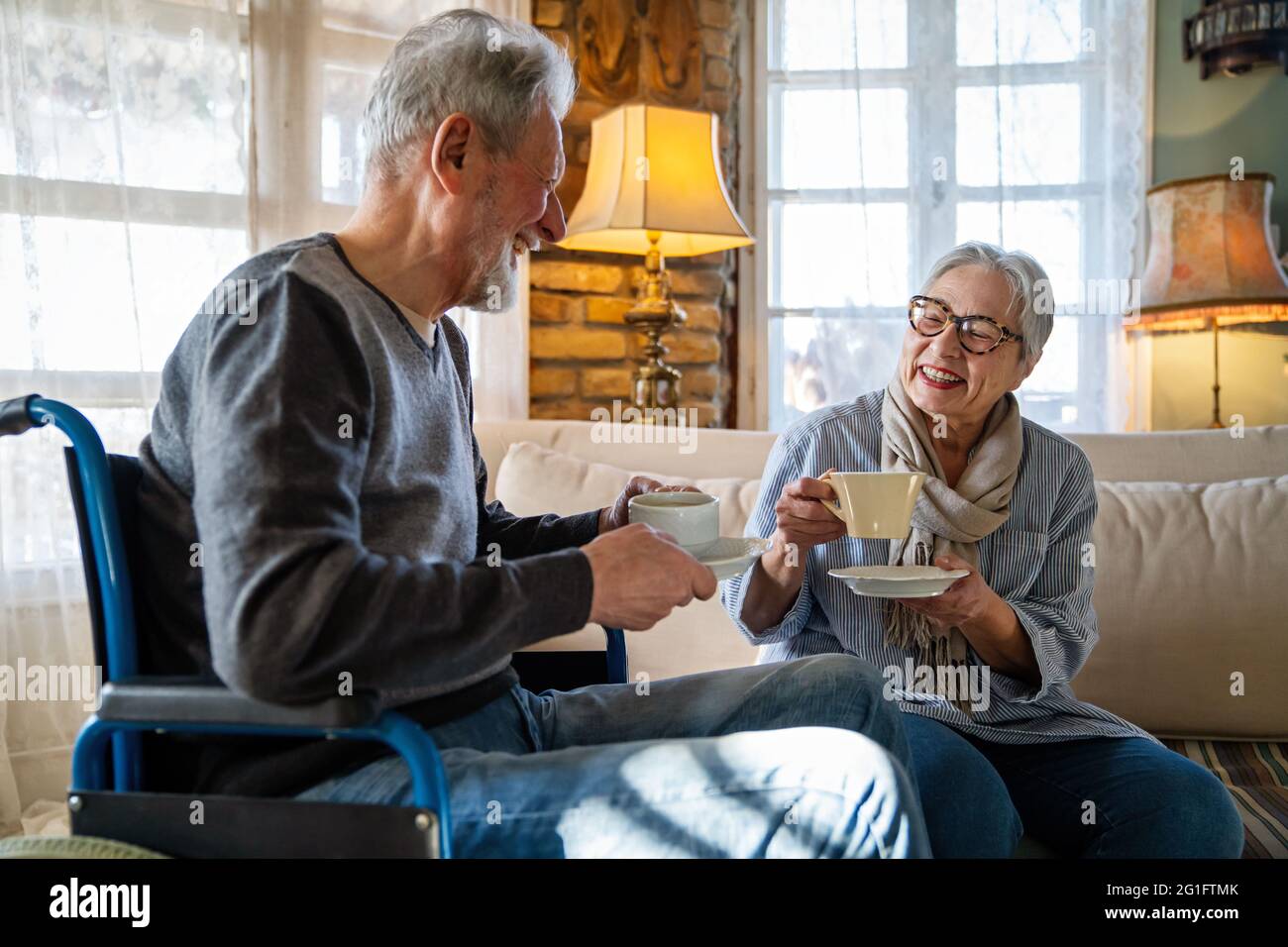 Mature man with disability in wheelchair. Happy retired senior couple having fun at home. Stock Photo