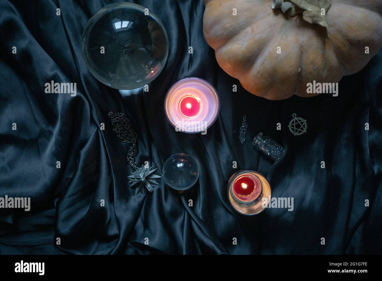 Witcher medallion, magical crystal ball, pumpkin and candles on the silk cloth. Magic, mystical theme, Witcher Netflix TV series concept Stock Photo
