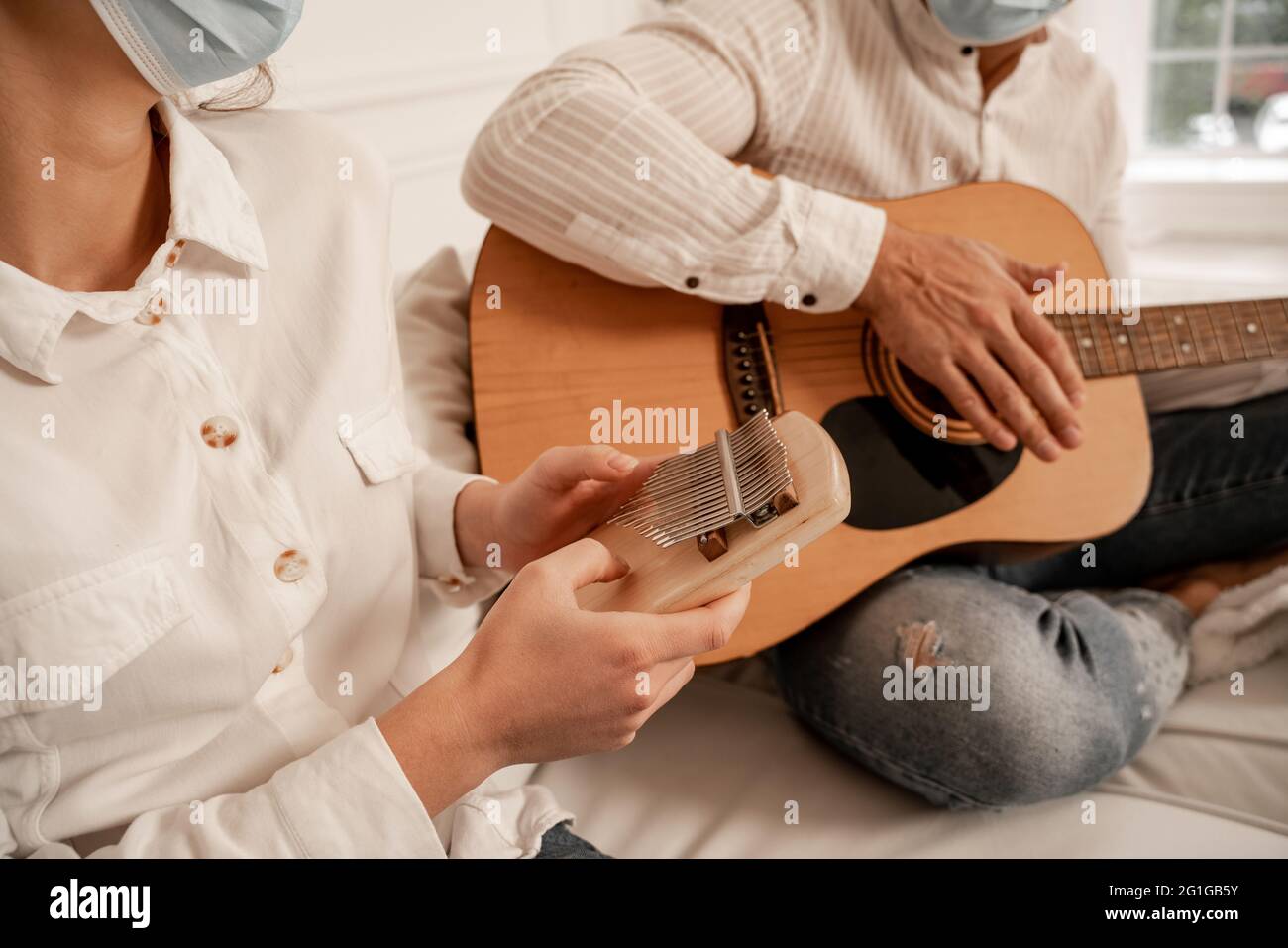 cropped view of couple in medical masks playing musical instruments at ...