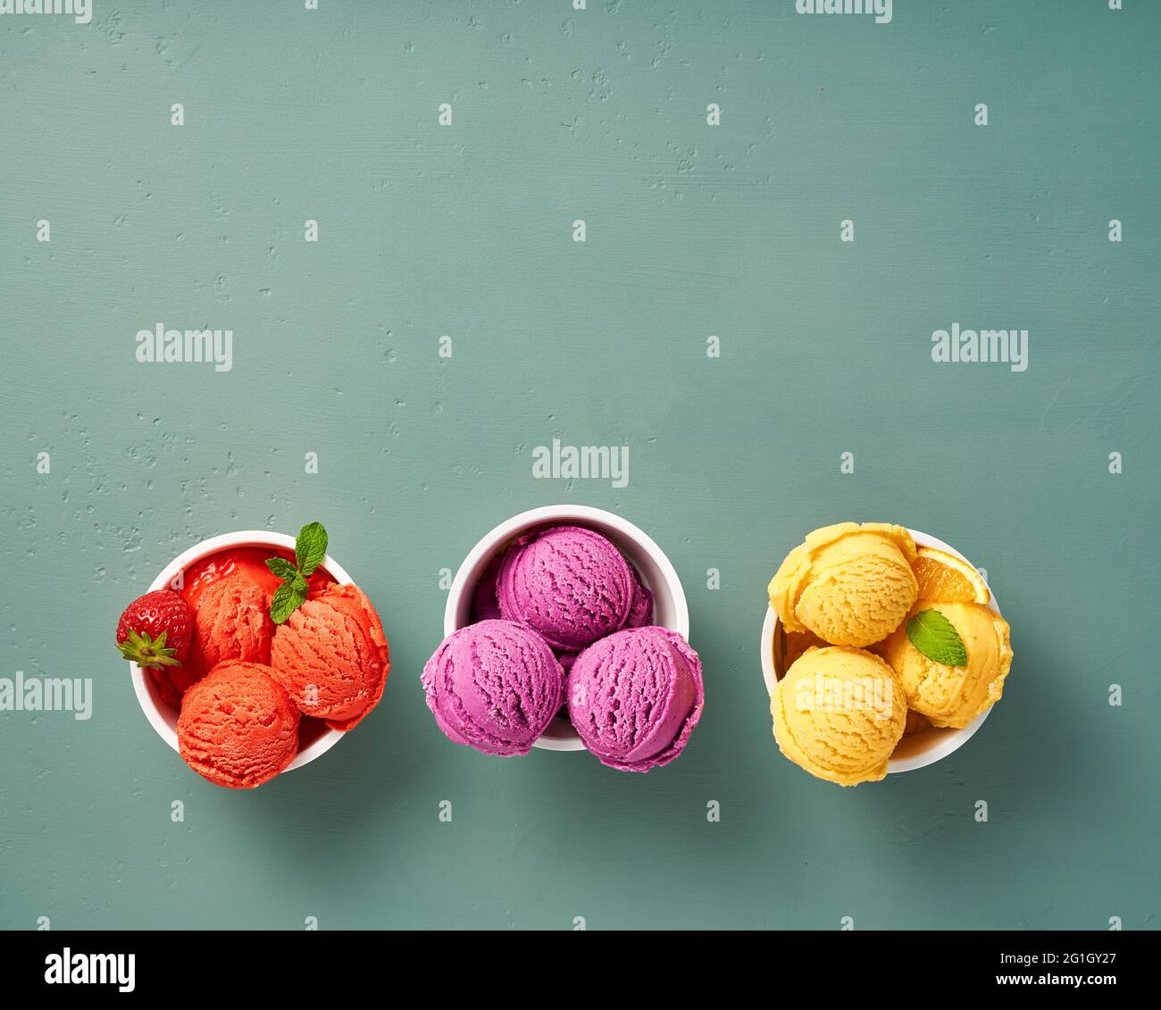 Gourmet flavours of Italian ice cream in vibrant colors served in individual paper cups on blue background. Strawberry sorbet, blueberry or lavender i Stock Photo