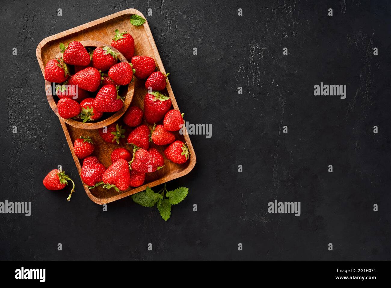 Fresh strawberry on a black concrete background. Strawberries with leaves on wooden plate. Stock Photo
