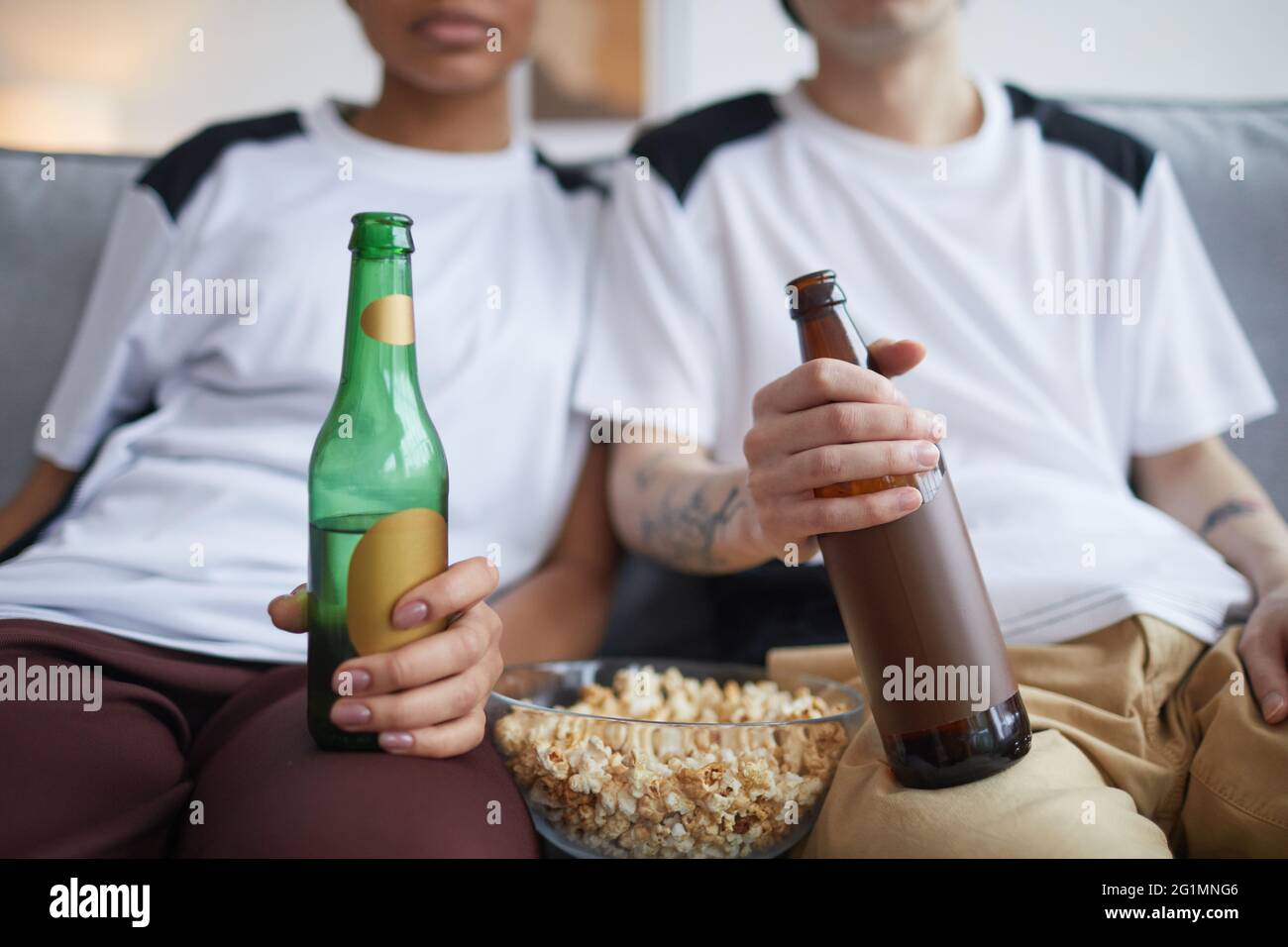 Close up of young couple watching TV or movies at home with focus on pop corn and beer bottles, copy space Stock Photo