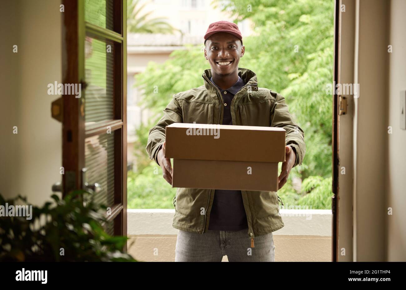 Smiling African delivery man holding packages at a front door Stock Photo