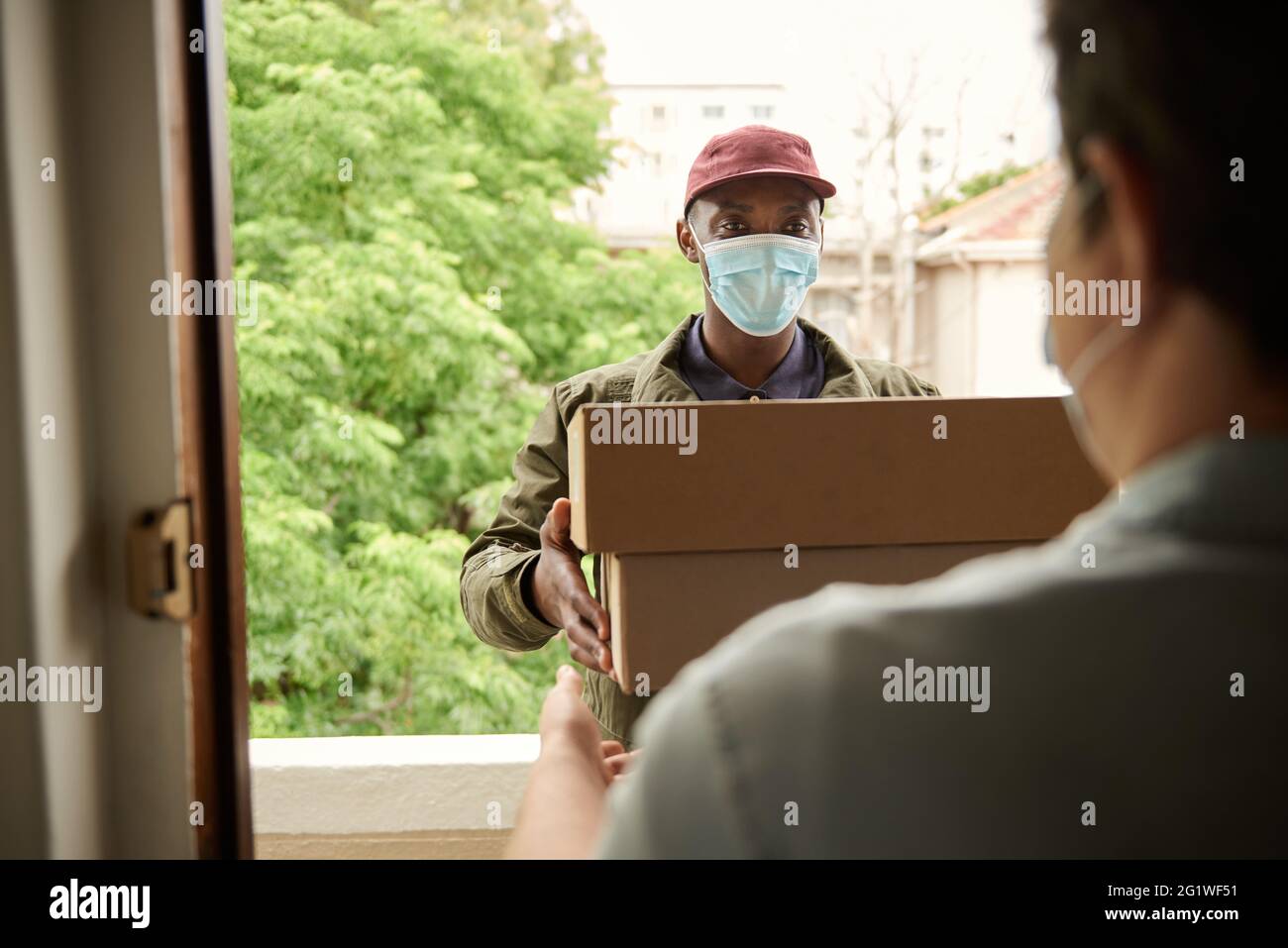 African courier in a mask giving packages to a customer Stock Photo